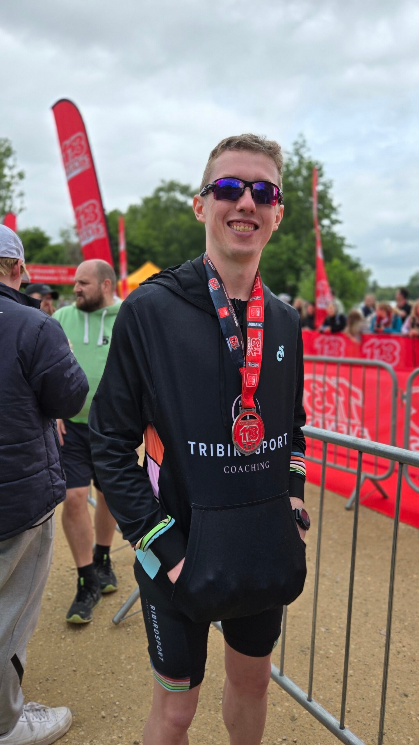 Ben, a Tribirdsport athlete, in a Tribirdsport Coaching hoodie and sunglasses with his race medal