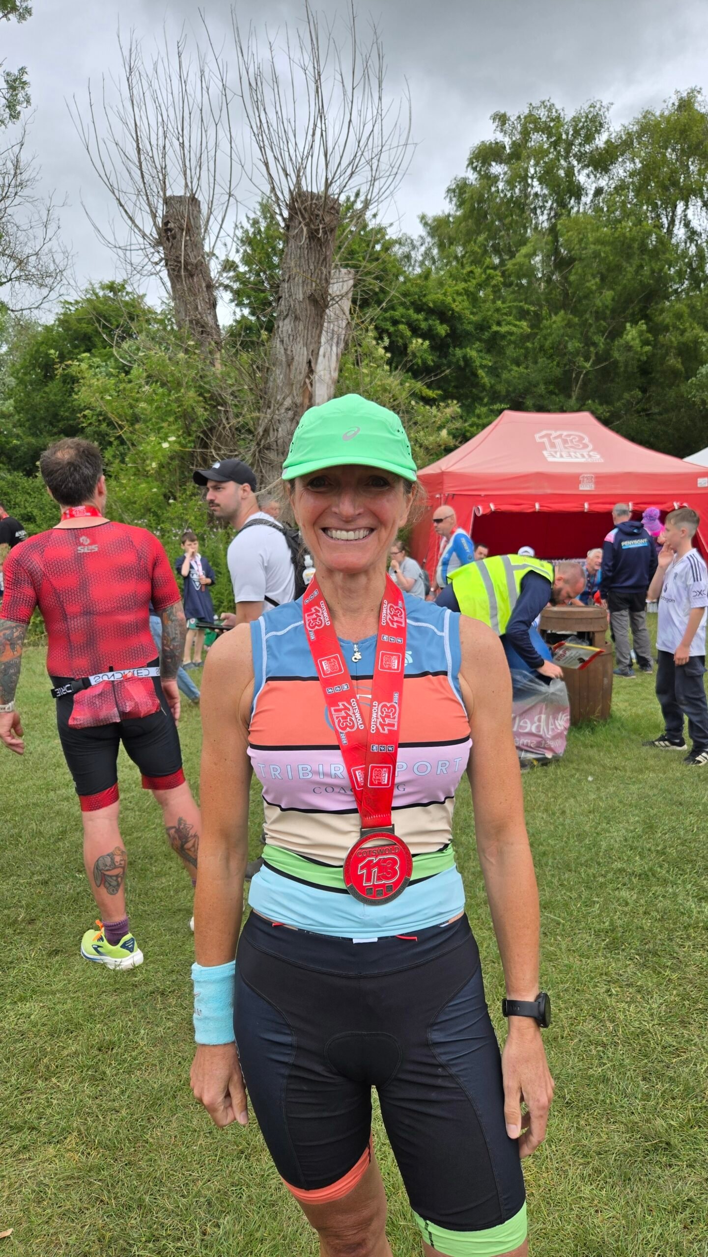 Donna, a Tribirdsport athlete, smiling in a green cap and striped tri suit with her race medal