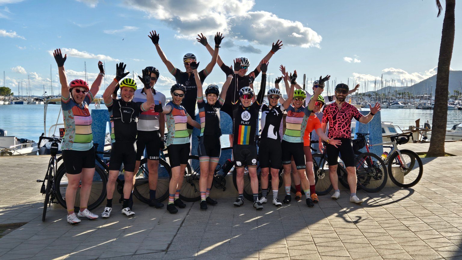 Tribirdsport camp group with their bikes, arms raised, beside the harbour in Mallorca