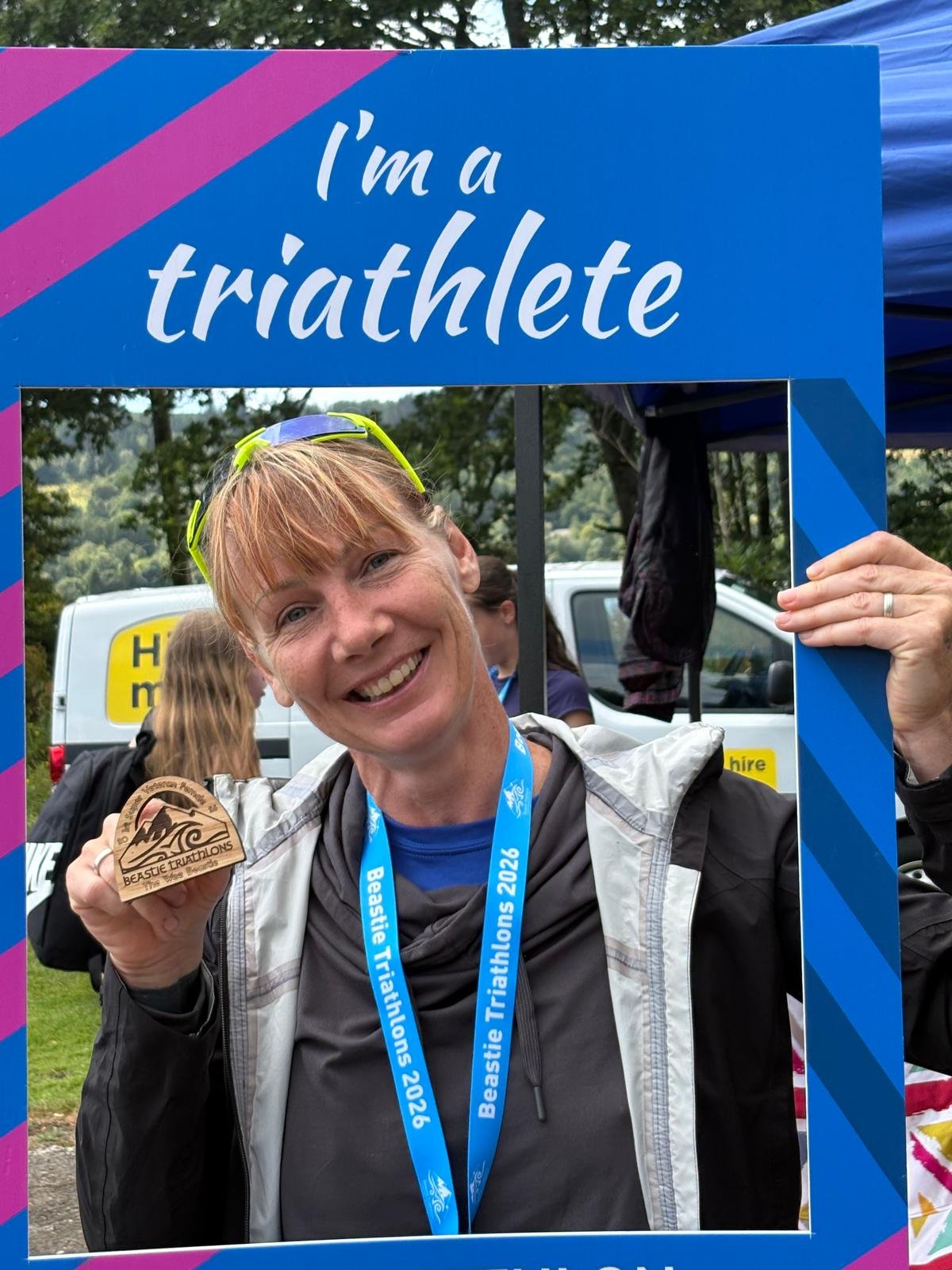 Clare, a Tribirdsport athlete, holding up her medal inside an ‘I’m a triathlete’ photo frame