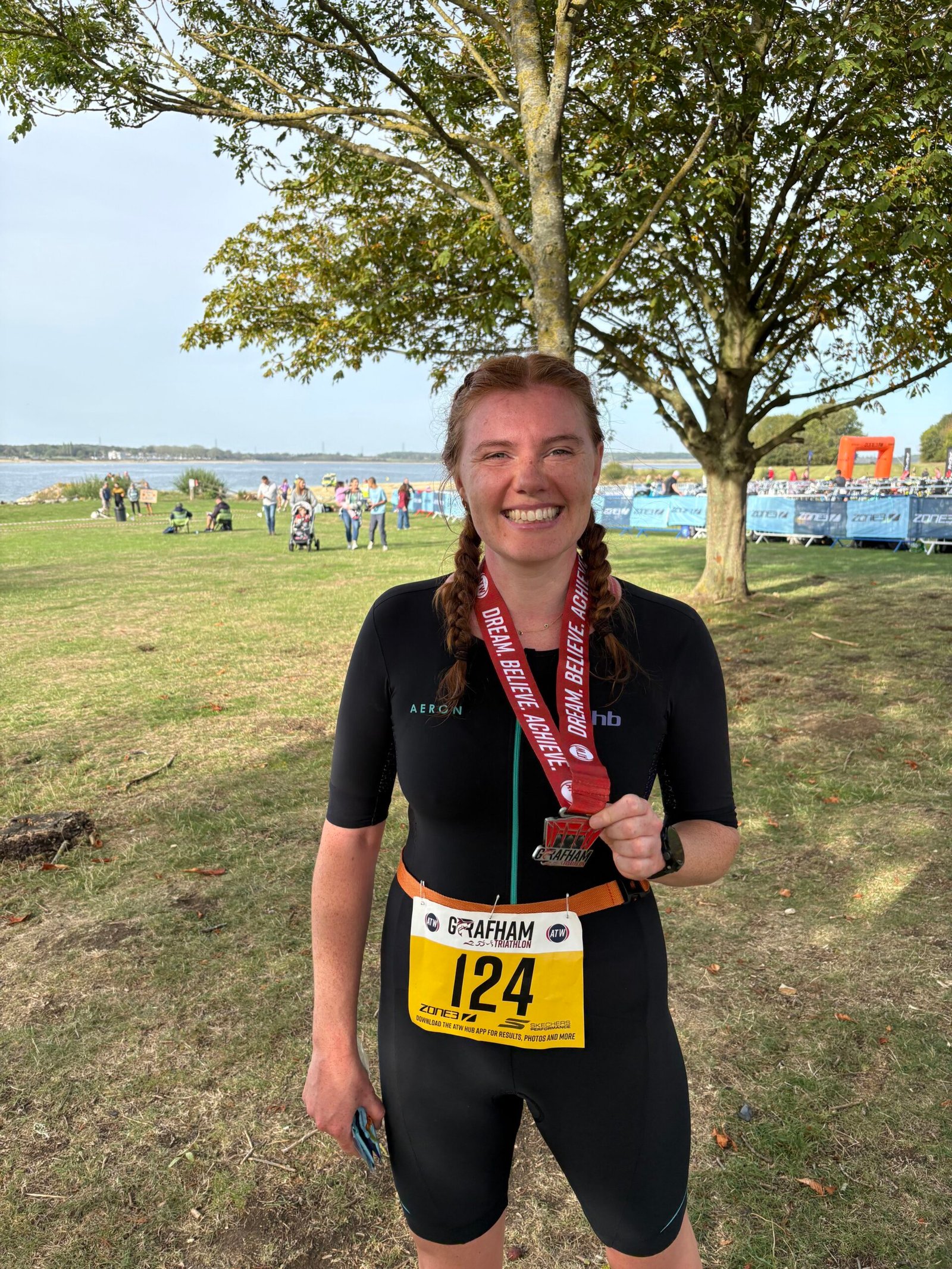 Ellie, a Tribirdsport athlete, smiling in her tri suit and race number with her medal